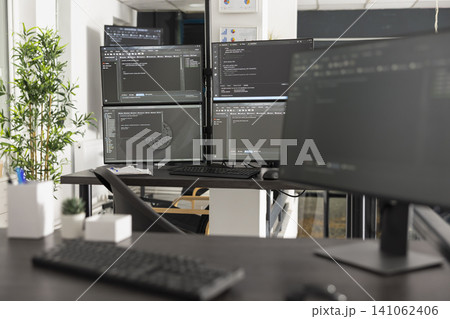 Empty office shows multiple computer screens filled with programming syntax and algorithms. Professional workspace represents web development, cybersecurity and digital business solutions. 141062406
