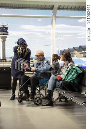 Smiling cabin crew member assisting elderly passenger with mobility aid, checking boarding pass and giving directions at airport terminal. Senior couple represents inclusive tourism. Smiling cabin crew member assisting elderly passenger with mobility aid, checking boarding pass and giving directions at airport terminal. Senior couple represents inclusive tourism. 141062442