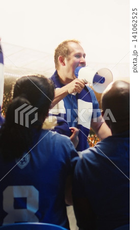 Vertical video Back view of fan leader standing with megaphone in packed soccer arena, chanting. Rear view of fans in stadium singing behind shouting football supporter Vertical video Back view of fan leader standing with megaphone in packed soccer arena, chanting. Rear view of fans in stadium singing behind shouting football supporter 141062525