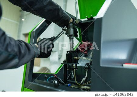 Mechanic hand in glove tightening diesel fuel injector with wrench tool on test bench for calibration in repair workshop 141062842