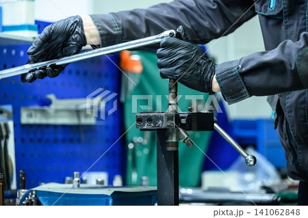 Mechanic hand in glove unscrewing common rail diesel fuel injector with long wrench bar on clamp holder in workshop Mechanic hand in glove unscrewing common rail diesel fuel injector with long wrench bar on clamp holder in workshop 141062848