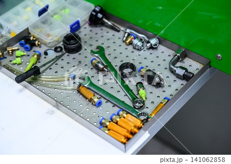 Diagnostic adapters quick couplers and wrench tools on perforated metal tray of test bench for fuel injector calibration Diagnostic adapters quick couplers and wrench tools on perforated metal tray of test bench for fuel injector calibration 141062858