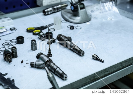 Disassembled old dirty used common rail fuel injector parts and internal components on workshop workbench table for repair Disassembled old dirty used common rail fuel injector parts and internal components on workshop workbench table for repair 141062864