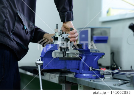 Mechanic hand disassembling common rail high pressure diesel fuel pump unit on metal vice clamp holder in service workshop Mechanic hand disassembling common rail high pressure diesel fuel pump unit on metal vice clamp holder in service workshop 141062883