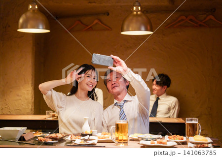 居酒屋で自撮りをする高齢男性と若い女性 141063785