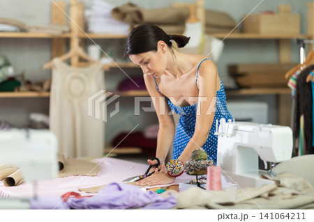 Woman seamstress cutting fabric in sewing workshop Woman seamstress cutting fabric in sewing workshop 141064211