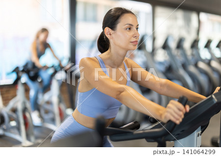 Smiling young girl doing spin bike exercises in well-equipped gym Smiling young girl doing spin bike exercises in well-equipped gym 141064299