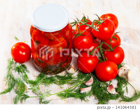 Jar with pickled tomatoes, dill, garlic and ripe tomatoes on the table 141064381