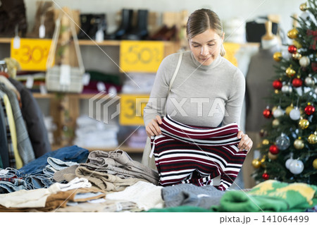 Uncertain young woman choosing sweater in clothing store Uncertain young woman choosing sweater in clothing store 141064499