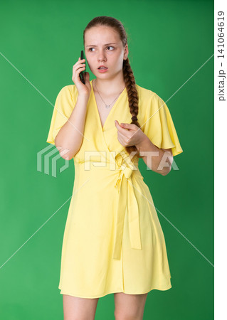 Teenage girl talking on mobile phone on green background. Teenage girl talking on mobile phone on green background. 141064619