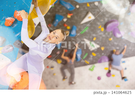 Adult woman practicing rock climbing on climbing wall 141064625