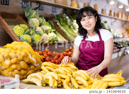 Friendly saleswoman puts fresh bananas on supermarket shelves Friendly saleswoman puts fresh bananas on supermarket shelves 141064630