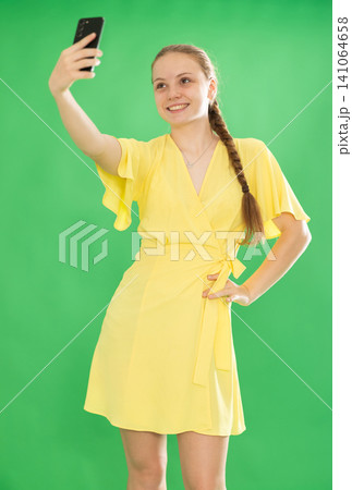 Teenage girl taking selfie in front of green screen 141064658