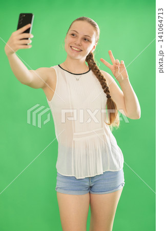 Teenage girl taking selfie in front of green screen Teenage girl taking selfie in front of green screen 141064713