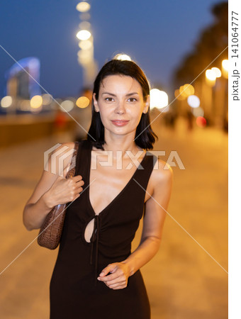 Young woman strolling along the evening promenade with city lights 141064777