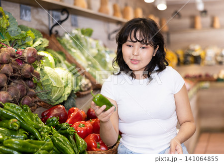 Portrait of positive satisfied girl buying bell peppers in grocery shop Portrait of positive satisfied girl buying bell peppers in grocery shop 141064855
