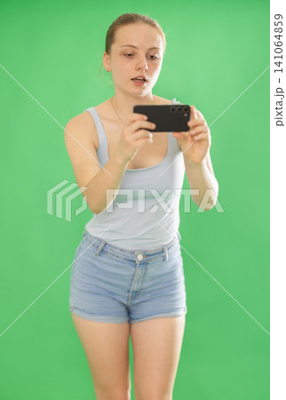Teenage girl in blue top takes photo or scans QR code with a smartphone. Chroma key compositing Teenage girl in blue top takes photo or scans QR code with a smartphone. Chroma key compositing 141064859