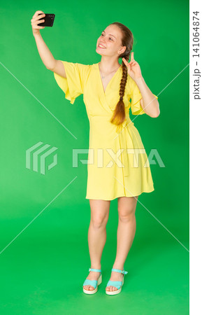 Teenage girl taking selfie in front of green screen 141064874
