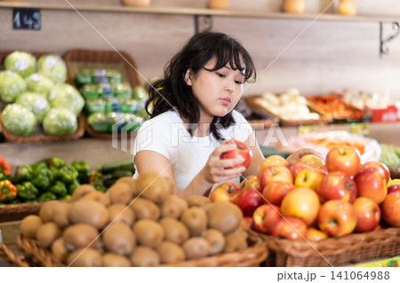 Happy smiling girl making purchases in supermarket, choosing fresh apples 141064988