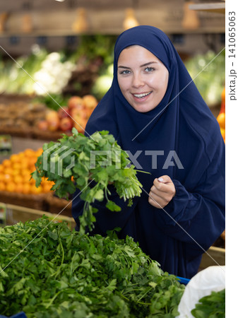 Young european woman in islamic dress choosing greens at market Young european woman in islamic dress choosing greens at market 141065063