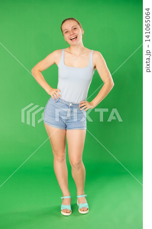 Portrait of teenage girl in blue top expressing happy emotions on green background 141065064