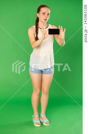Teenage girl taking photo or scanning QR code in front of green screen 141065106