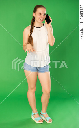 Teenage girl talking on mobile phone in front of green screen Teenage girl talking on mobile phone in front of green screen 141065123