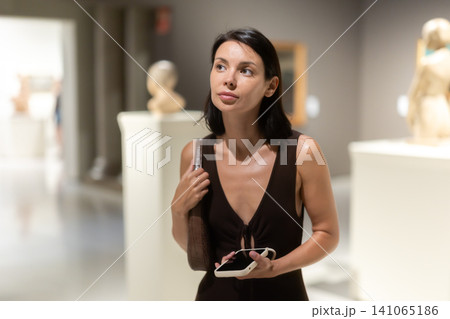 Woman with phone in hands in museum hall, view statues exhibition. Woman with phone in hands in museum hall, view statues exhibition. 141065186