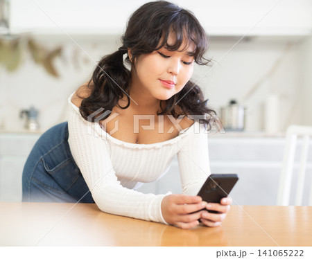 Smiling girl texting on her smartphone at living room 141065222