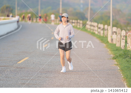 Active young Asian woman jogging and running in the public park at morning. female athlete in sportswear exercising for healthy lifestyle and fitness workout outdoors. Wellness and sport concepts Active young Asian woman jogging and running in the public park at morning. female athlete in sportswear exercising for healthy lifestyle and fitness workout outdoors. Wellness and sport concepts 141065412