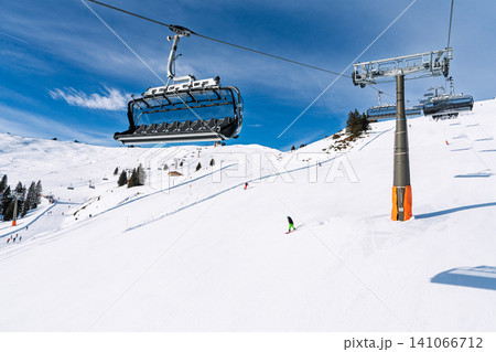 Ski lift and skiers on a sunny winter slope in Saalbach Hinterglemm, Austria, Alps landscape Ski lift and skiers on a sunny winter slope in Saalbach Hinterglemm, Austria, Alps landscape 141066712