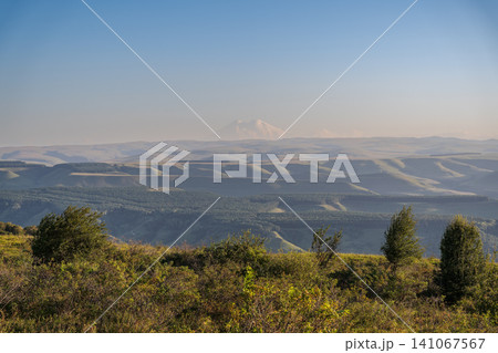 Panoramic view of the green valley and the snowy peak of Mount Elbrus on the horizon against the blue sky on a sunny clear morning in Kislovodsk Stavropol territory, Russia Panoramic view of the green valley and the snowy peak of Mount Elbrus on the horizon against the blue sky on a sunny clear morning in Kislovodsk Stavropol territory, Russia 141067567