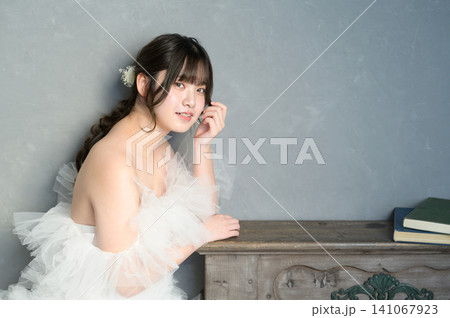 グレー背景で頬杖をつき微笑むウェディングドレスの日本人女性 グレー背景で頬杖をつき微笑むウェディングドレスの日本人女性 141067923