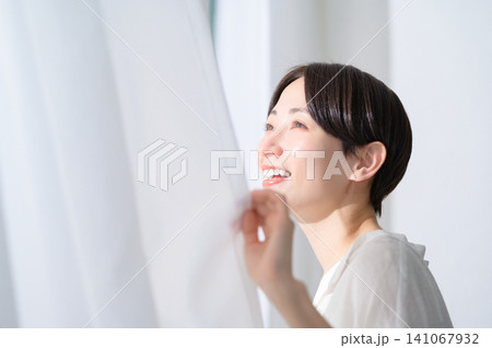 カーテンを開けて朝日を浴びる日本人女性のビューティイメージ 141067932