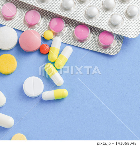 Colorful medical tablets and capsules spilled from a blister pack on blue surface Colorful medical tablets and capsules spilled from a blister pack on blue surface 141068048