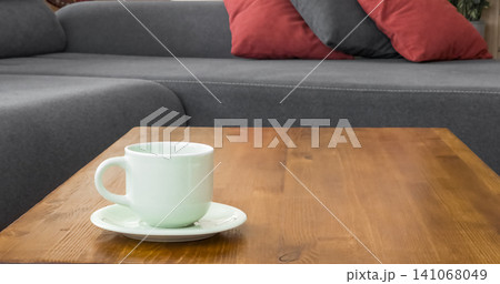 Ceramic coffee cup on a wooden table near a sofa left side Ceramic coffee cup on a wooden table near a sofa left side 141068049