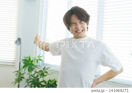 窓際でストレッチをする痛い顔の若い日本人男性 窓際でストレッチをする痛い顔の若い日本人男性 141069271