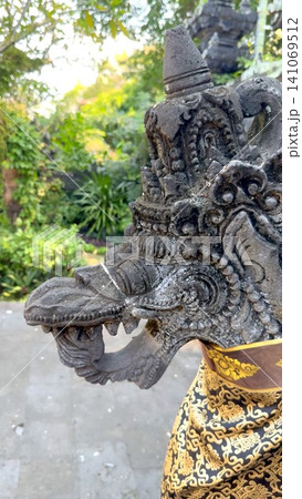 Weathered stone dragon head carving with decorative cloth on temple structure in tranquil garden setting, showing ornate patterns, moss patina, and aged stone texture Weathered stone dragon head carving with decorative cloth on temple structure in tranquil garden setting, showing ornate patterns, moss patina, and aged stone texture 141069512