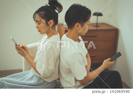 背中合わせでそれぞれスマホを見るカップル 背中合わせでそれぞれスマホを見るカップル 141069590