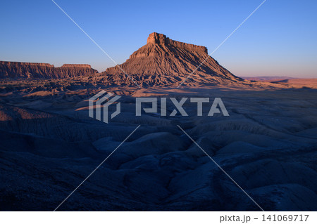 Peaceful majestic mountain peak rises above dark shadow valley during beautiful golden sunrise sunlight across vast dry desert landscape of wild utah nature environment evoking profound awe Peaceful majestic mountain peak rises above dark shadow valley during beautiful golden sunrise sunlight across vast dry desert landscape of wild utah nature environment evoking profound awe 141069717