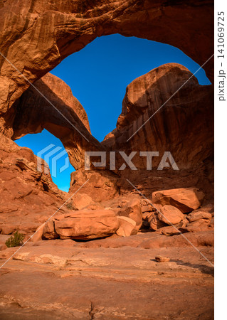 Majestic natural rock arch formation framing bright blue sky in an awe inspiring peaceful red sandstone utah desert landscape showcasing magnificent geological wonder 141069725