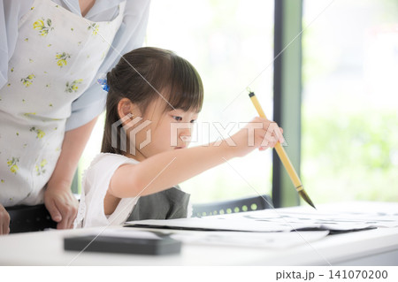 書道に集中して筆で文字を書く小学生の女の子・習字を学ぶ日本の子ども 真剣な表情で先生に教わる 書道に集中して筆で文字を書く小学生の女の子・習字を学ぶ日本の子ども 真剣な表情で先生に教わる 141070200