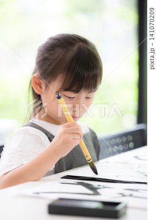 書道に集中して筆で文字を書く小学生の女の子・習字を学ぶ日本の子ども　真剣な表情の縦クローズアップ 141070209