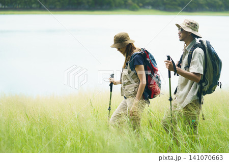 Couple hiking with backpacks near lake. Outdoor adventure and travel lifestyle. 141070663