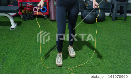 Cropped view of woman jumping rope on green turf in gym for cardio workout 141070960
