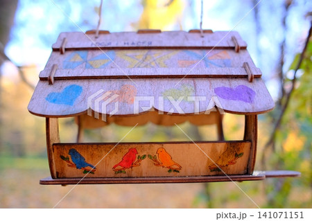 Handcrafted wooden bird feeder suspended outdoors in a park Handcrafted wooden bird feeder suspended outdoors in a park 141071151