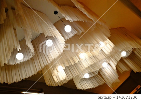 Cream fabric layers drape from the ceiling, lit by bright spherical pendant lights Cream fabric layers drape from the ceiling, lit by bright spherical pendant lights 141071230