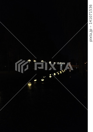 Luminous umbrella lights line a waterfront path at night Luminous umbrella lights line a waterfront path at night 141071536