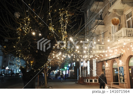 Bare trees with golden string lights line an urban street, illuminating buildings Bare trees with golden string lights line an urban street, illuminating buildings 141071564