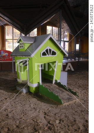 A bright green wooden playhouse with white trim and a grey roof stands on sand A bright green wooden playhouse with white trim and a grey roof stands on sand 141071622